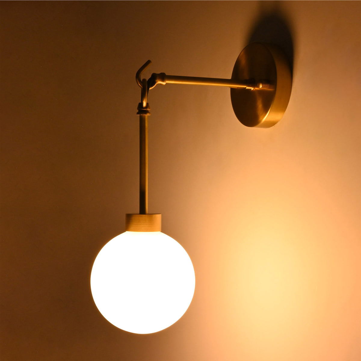 Side view of the Windsor Modern Brass Globe Wall Sconce installed on a wall, showcasing its decorative brass arm, suspended globe, and warm ambient glow.