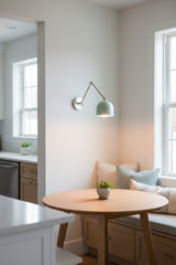 Adjustable bedside wall sconce with white dome shade, movable brass arm, and round wall canopy for modern interiors