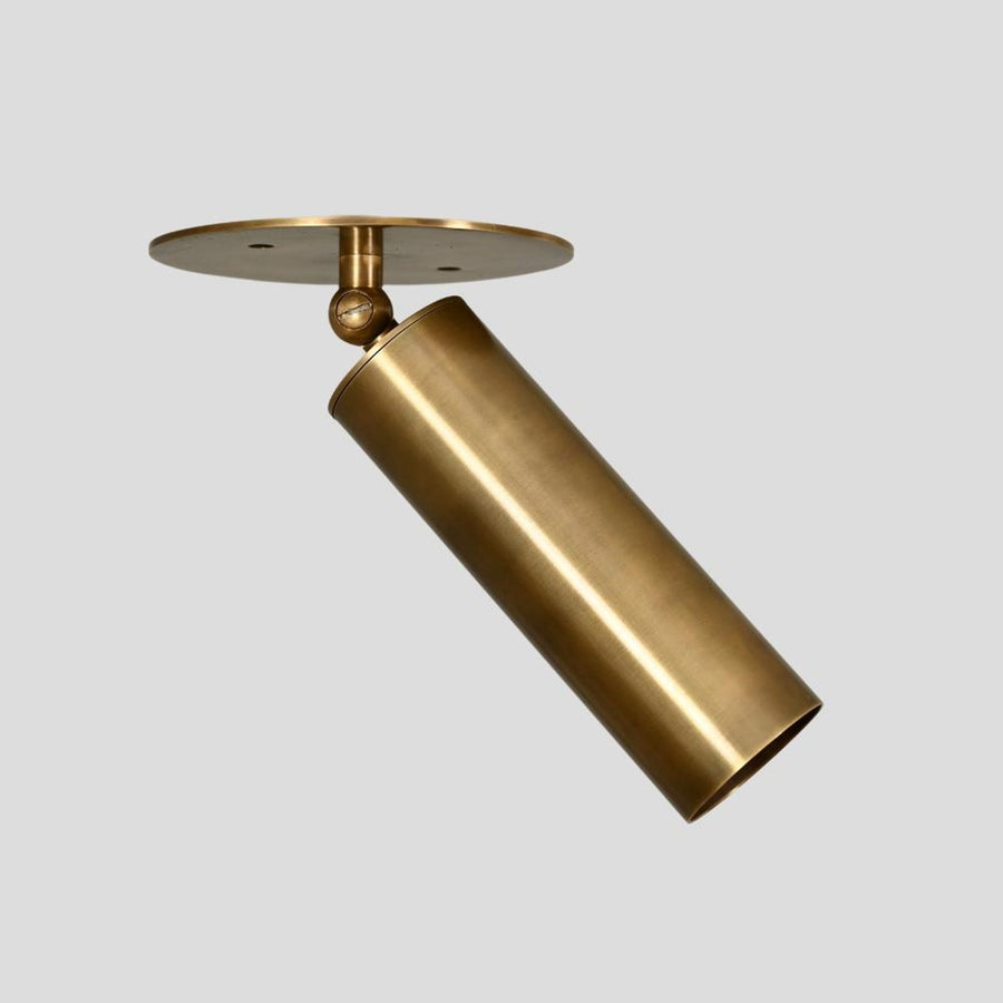 Adjustable brass cylinder spotlight with ceiling mount, handmade industrial minimalist design, side angle view.