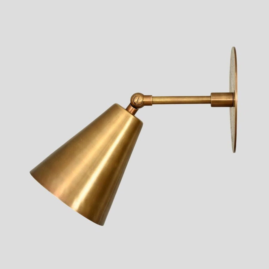Adjustable brass wall sconce with cone shade, handmade minimalist industrial design, side view.