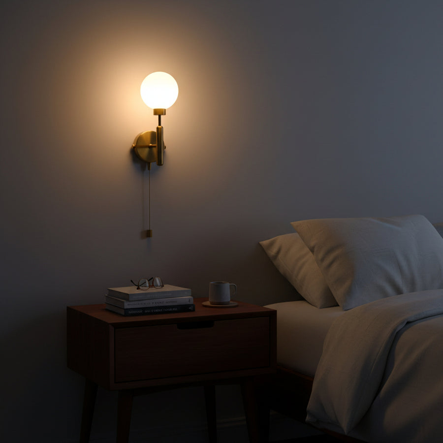 Modern brass globe wall light with round canopy, vertical stem, pull chain control, and soft warm ambient illumination