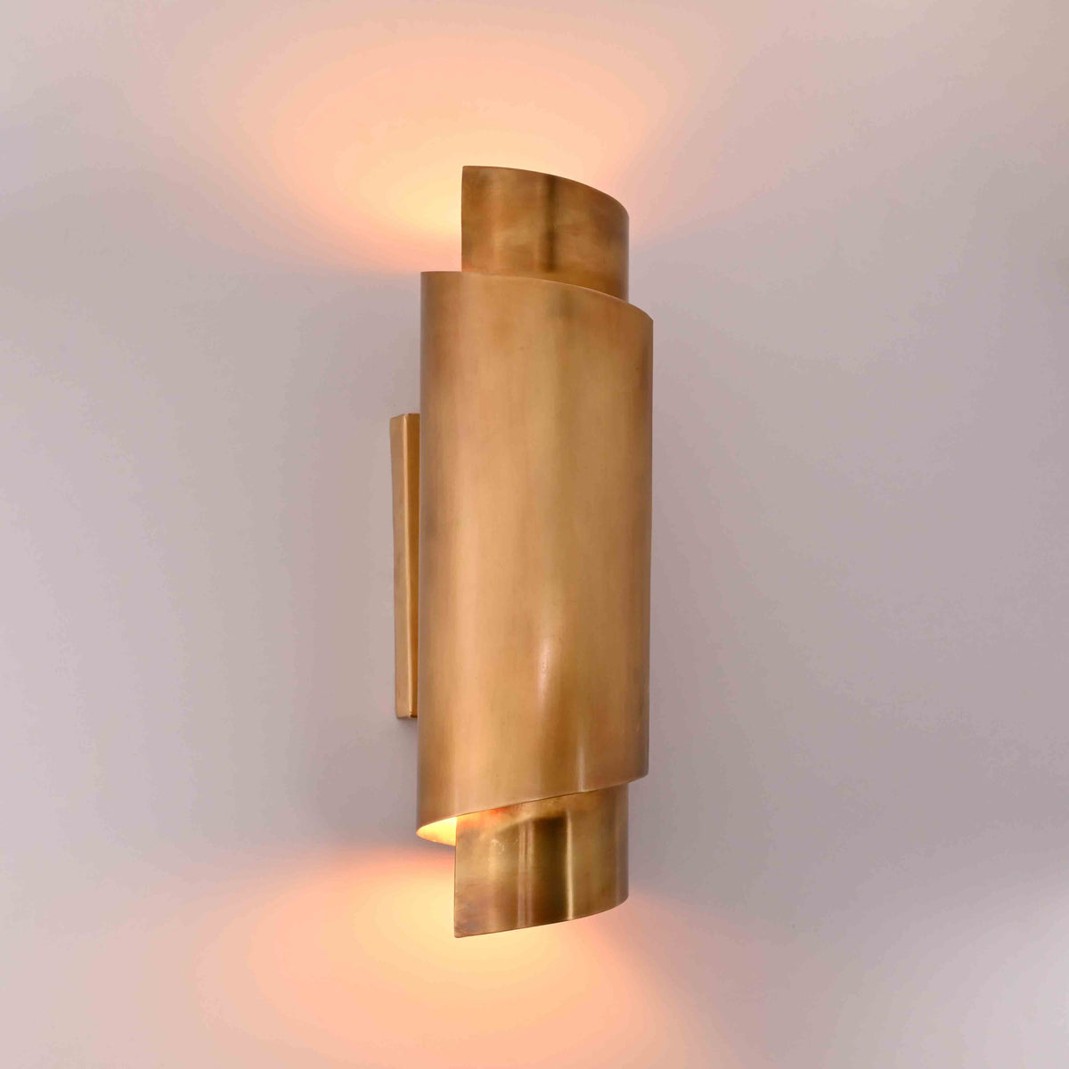 Modern brass wall light closeup showing sculptural curved shade and warm side glow detail
