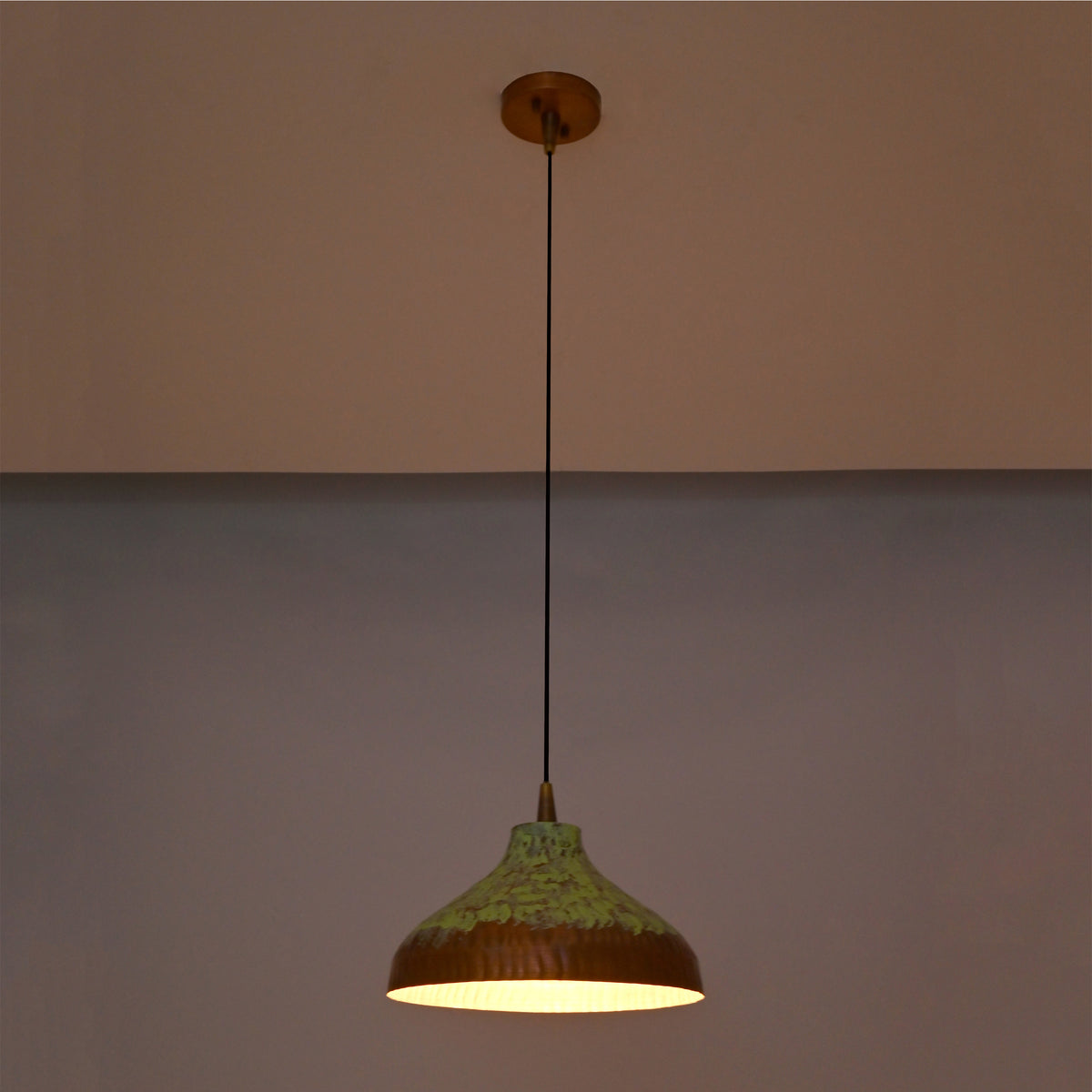 Artistic copper hanging pendant light with green patina finish, black suspension cord, and wide shallow dome shade