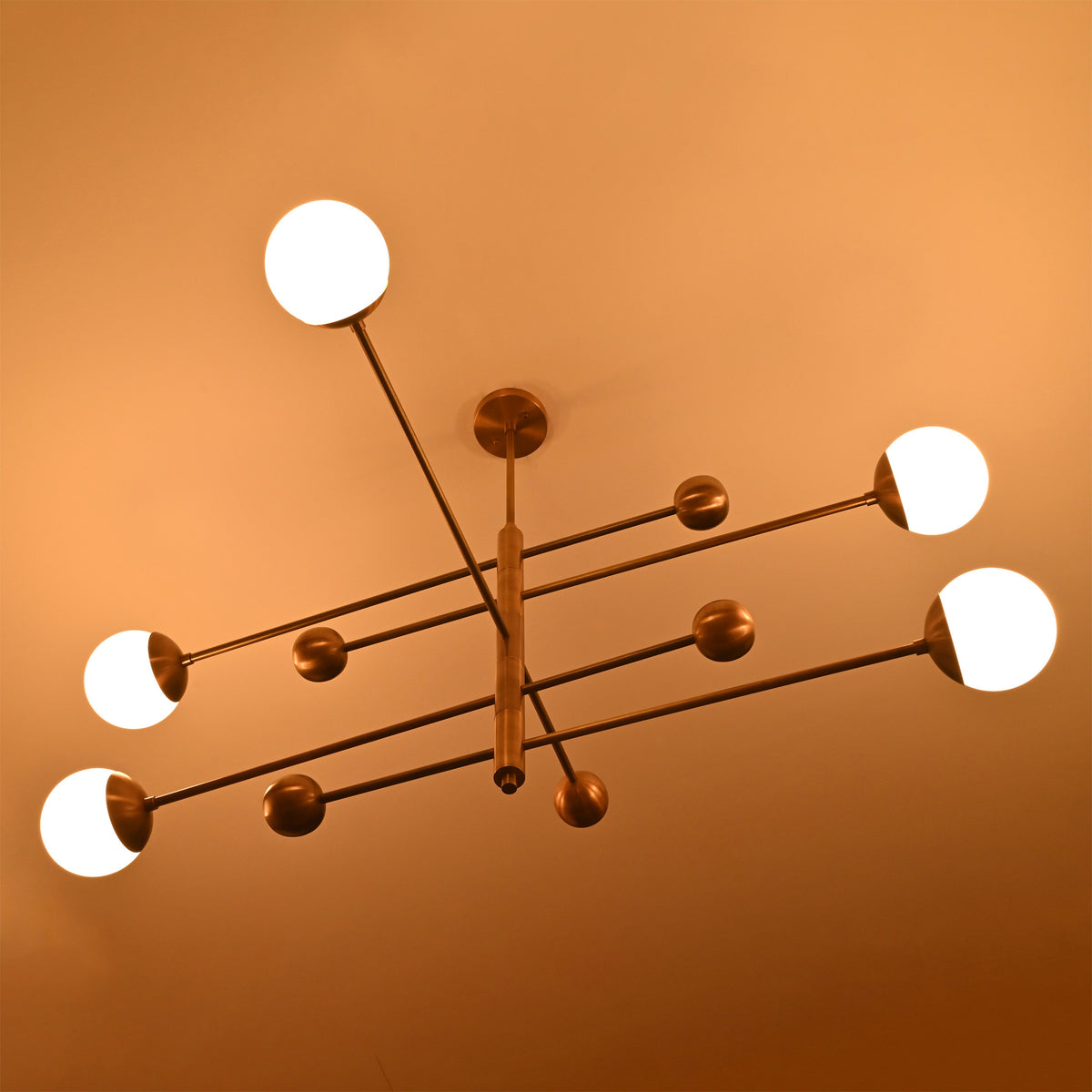 Aurelia brass ceiling light with five glowing globe shades, long horizontal rods, and decorative sphere accents