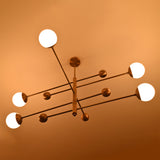 Aurelia brass ceiling light with five glowing globe shades, long horizontal rods, and decorative sphere accents
