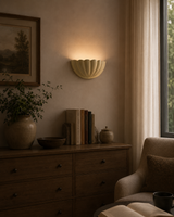 Aurora modern ivory fluted half bowl wall sconce installed in a contemporary living room, providing warm indirect ambient illumination above a wooden console table.