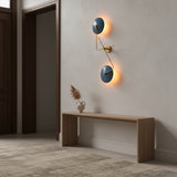 Closeup of backlit blue disc wall sconce showing warm ambient glow and sculptural brass detailing