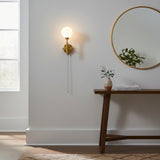 Bedside pull chain globe sconce with warm ambient lighting, raw brass finish, and compact wall-mounted design