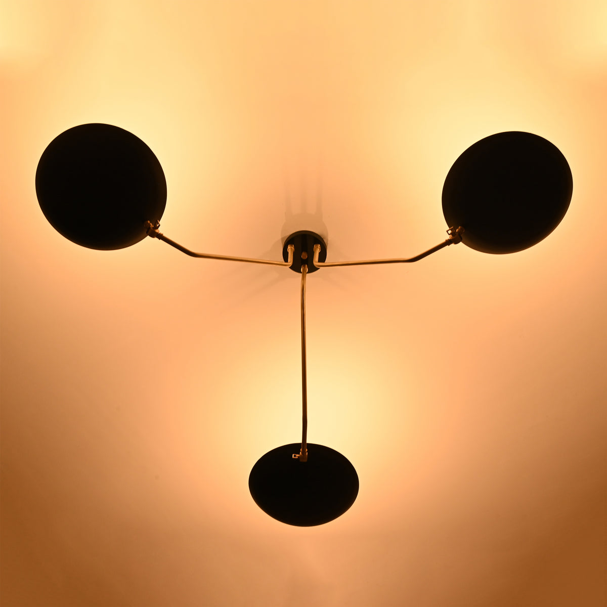 Bottom glowing view of black bowl chandelier illuminating the ceiling with warm ambient light and stylish brass arms.