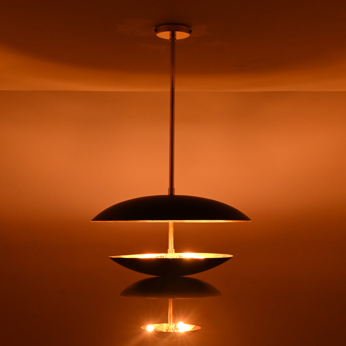 Black and brass disc chandelier showing illuminated lower bowl with soft diffused light