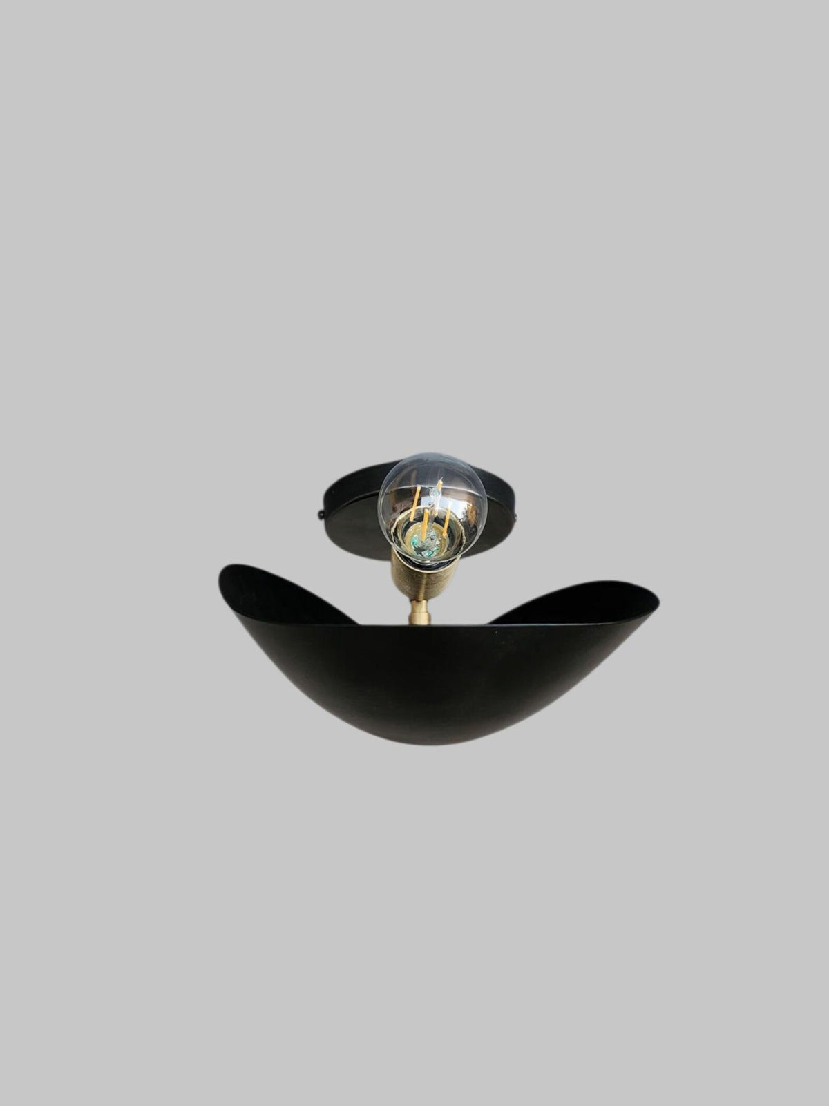 Front view of black brass leaf-shaped wall sconce with exposed bulb