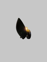 Black brass leaf-shaped wall sconce illuminated with warm glow