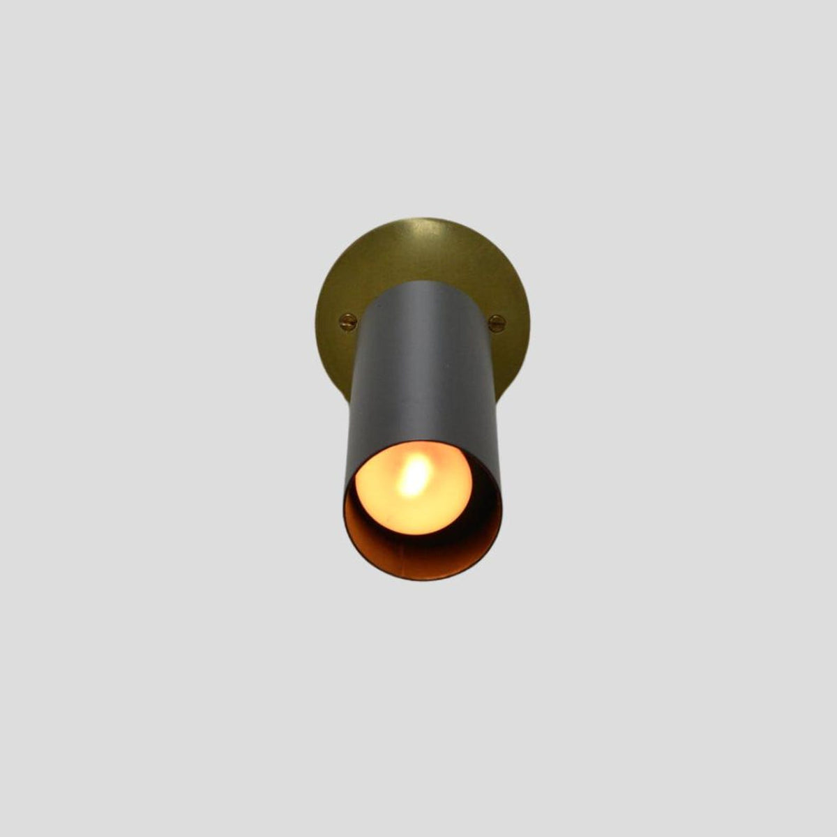 Modern black and brass spotlight with warm bulb glow, mounted on round brass base