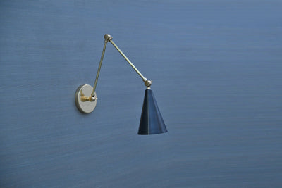 Black cone adjustable brass wall sconce with swing arm, mounted on blue wall