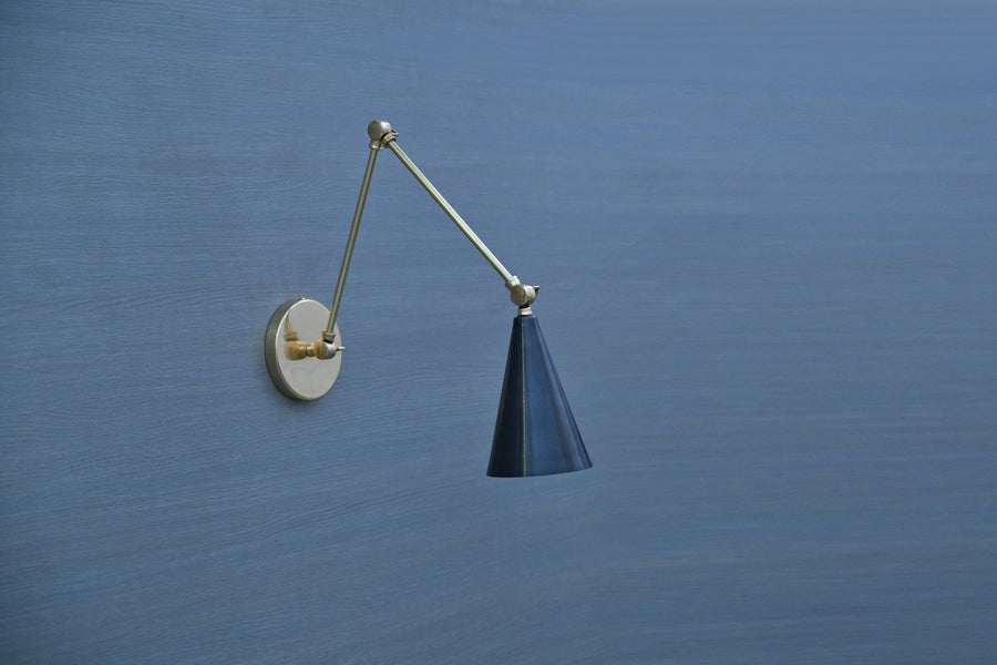 Black cone adjustable brass wall sconce with swing arm, mounted on blue wall