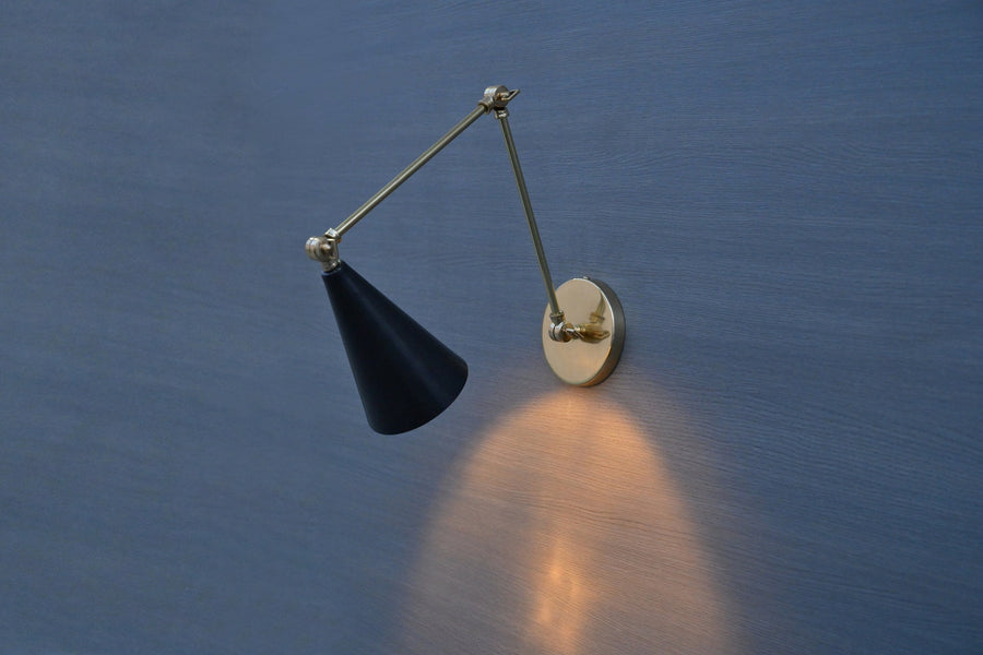Black cone adjustable brass wall sconce with swing arm, mounted on blue wall