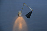 Adjustable brass wall lamp with black cone shade, projecting downward light