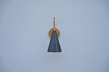 Front view of handcrafted brass wall sconce featuring a sleek black cone shade and warm brass frame