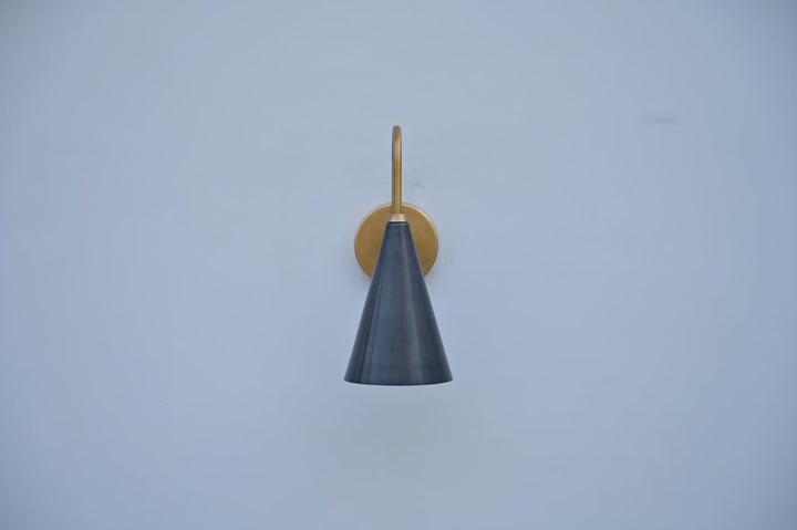 Front view of handcrafted brass wall sconce featuring a sleek black cone shade and warm brass frame