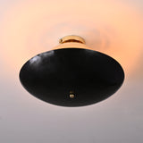 Bottom view of mixed-finish brass flushmount with blackened lower bowl and soft warm illumination from the polished brass upper dome.