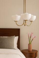 Solid brass 3-light bowl glass chandelier installed above a bed with soft ambient bedroom lighting