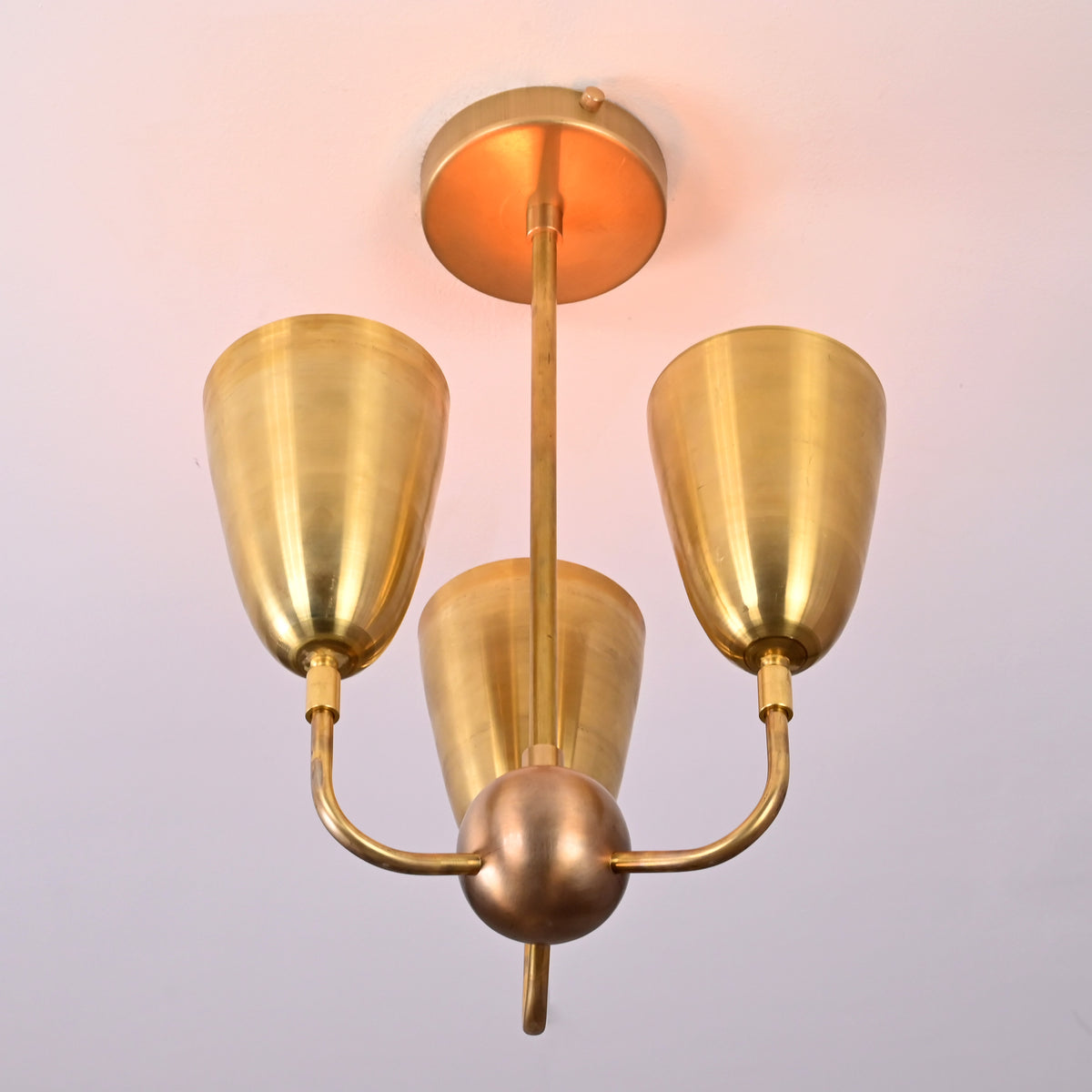 Bottom angle view of brass three-light ceiling fixture featuring sculpted cup shades and mid-century styling.