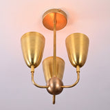 Bottom angle view of brass three-light ceiling fixture featuring sculpted cup shades and mid-century styling.