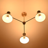 Soft glowing bottom view of brass 3-light chandelier with modern white bowl-shaped shades.