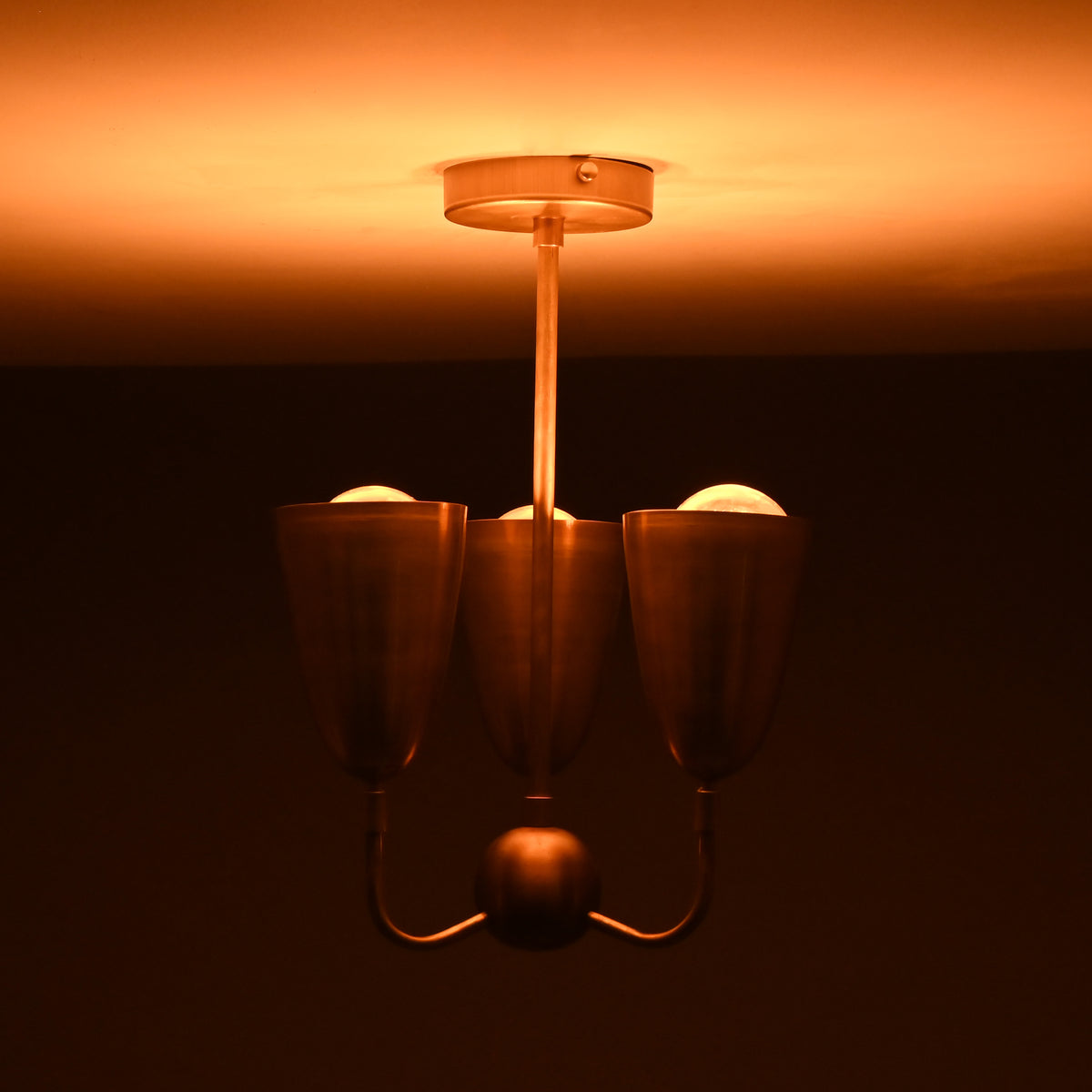 Brass 3-light chandelier emitting soft warm illumination, showcasing elegant cup shades and a minimalist brass stem.