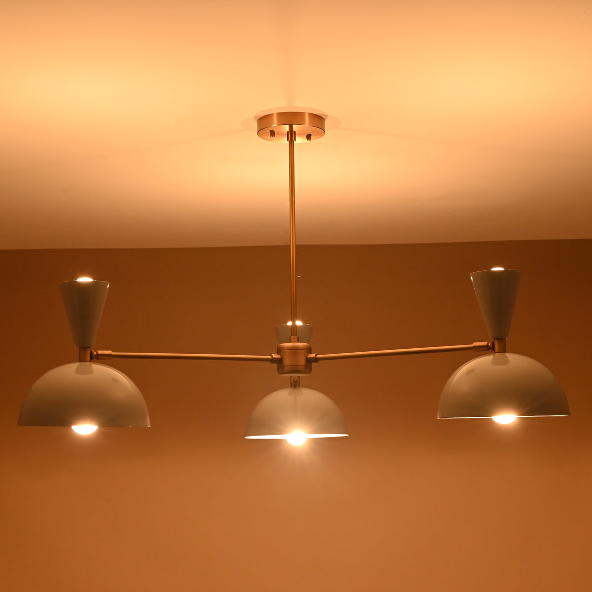 Mid-century brass 3-light chandelier emitting soft warm glow, handcrafted by Brass Leaf Studio.