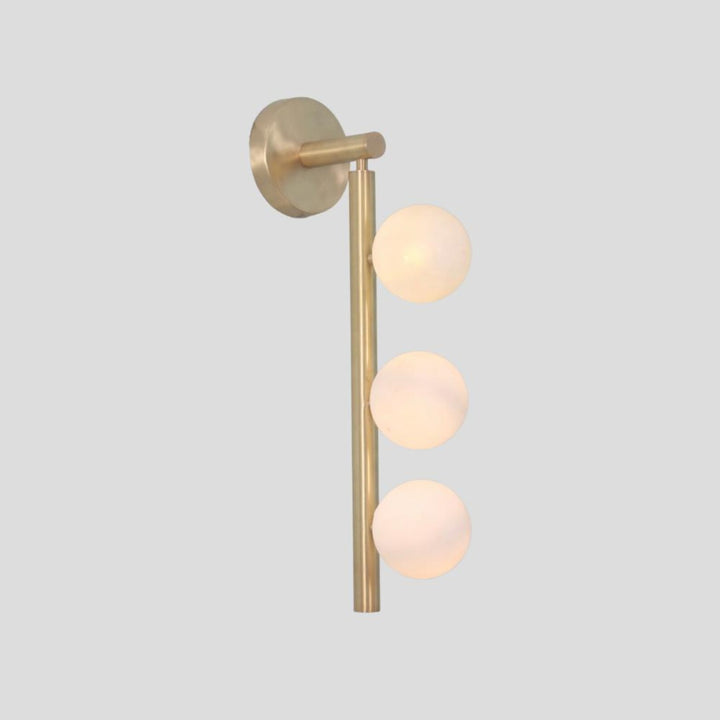 Vertical brass wall sconce with three frosted glass globes, modern minimalist lighting side angle