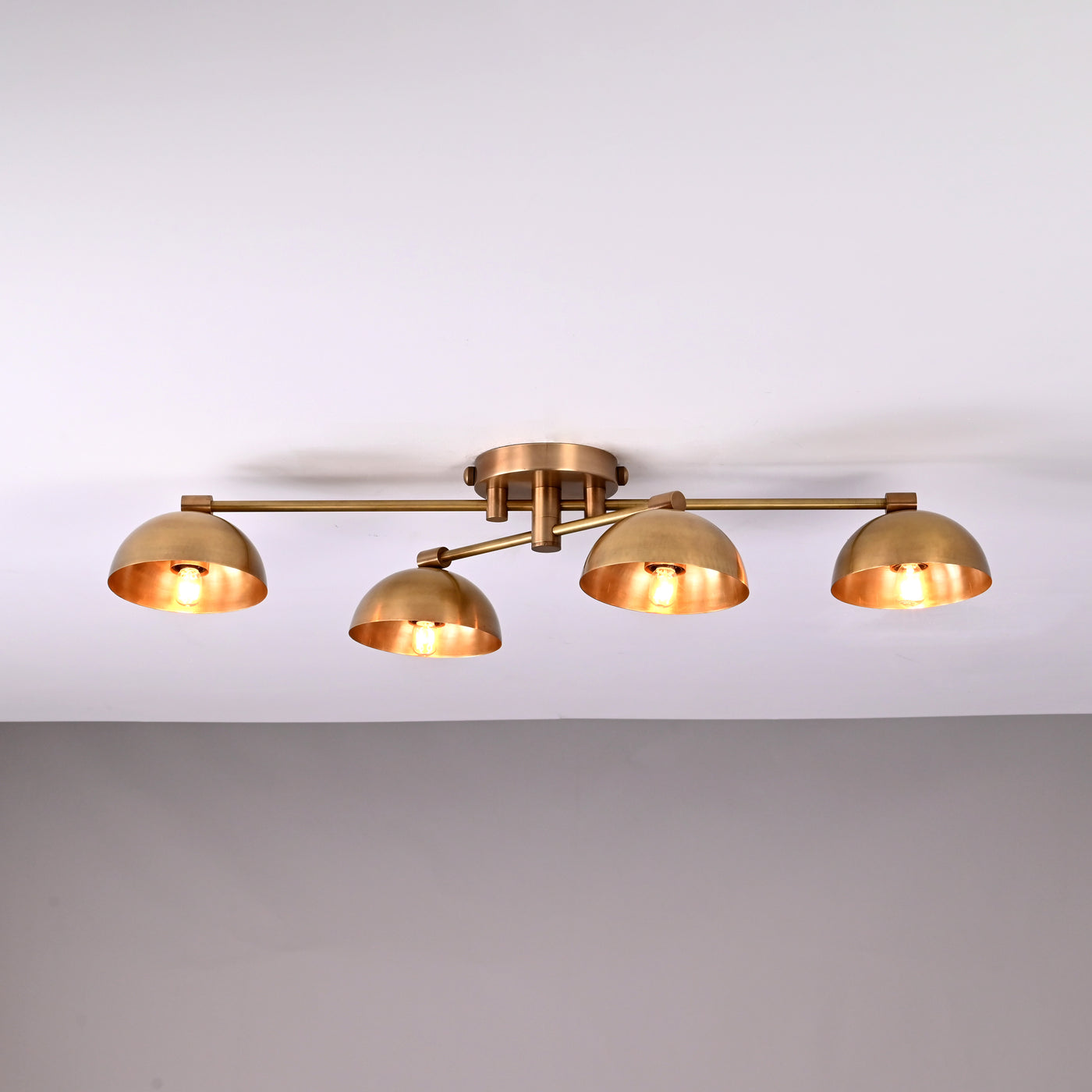 Handmade brass ceiling light with four dome-shaped shades illuminated, modern low-profile 4-light fixture for living room or hallway.
