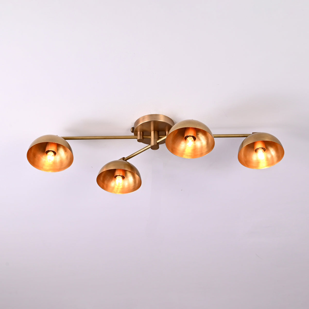 Contemporary 4-light brass flushmount chandelier featuring adjustable arms and warm glowing dome shades, minimalist ceiling light.