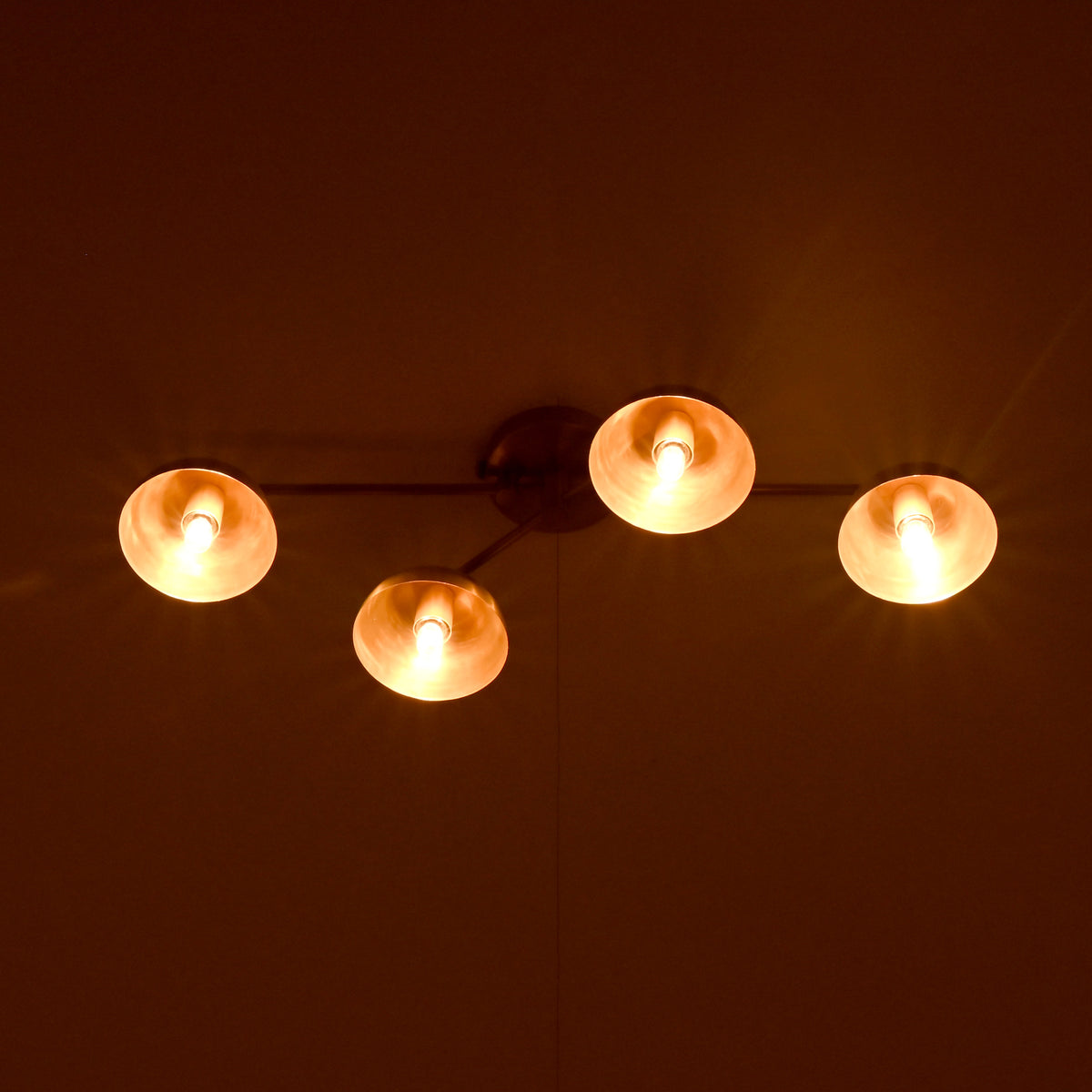 Brass 4-light ceiling fixture glowing warmly in a dark room, bowl shades casting soft ambient illumination.