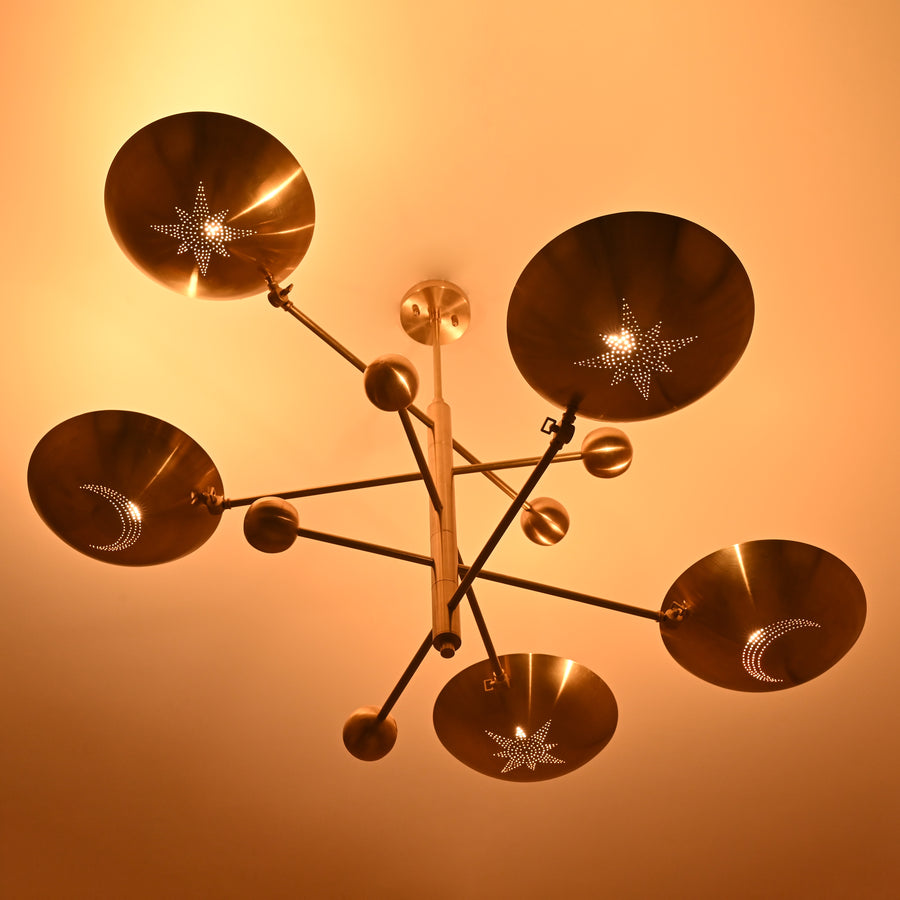 Celestial 5-light brass chandelier with star and moon perforated shades, handcrafted by Brass Leaf Studio.