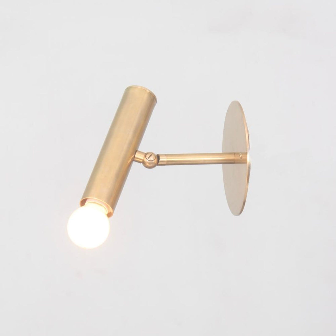 Brass adjustable wall spotlight with cylindrical body and round backplate, shown with glowing bulb