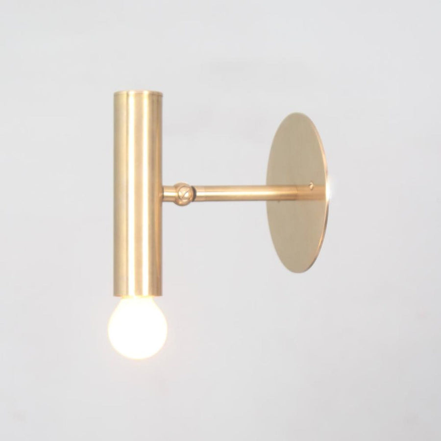 Brass adjustable wall spotlight with cylindrical body and round backplate, shown with glowing bulb