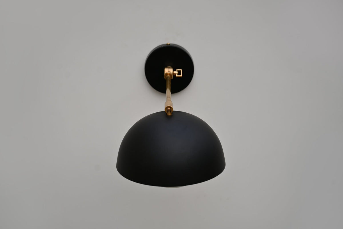 Top angle view of brass arm and matte black dome wall sconce showing clean geometry and handcrafted detailing.