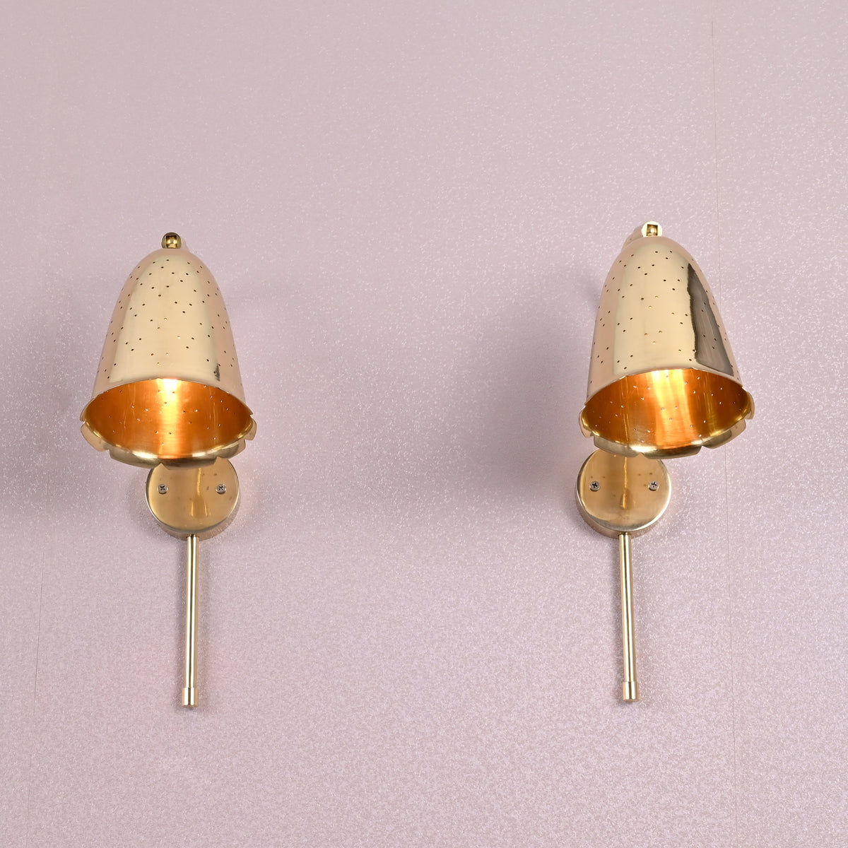 Front view of two brass bell wall sconces with perforated design and brushed brass finish