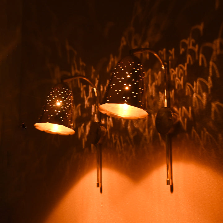 Two brass bell wall sconces glowing warmly, projecting ambient light patterns on textured wall