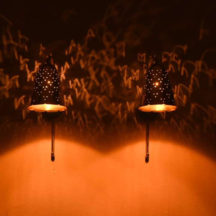 Brass bell wall sconces illuminated in a dark room, casting decorative perforated light patterns on the wall