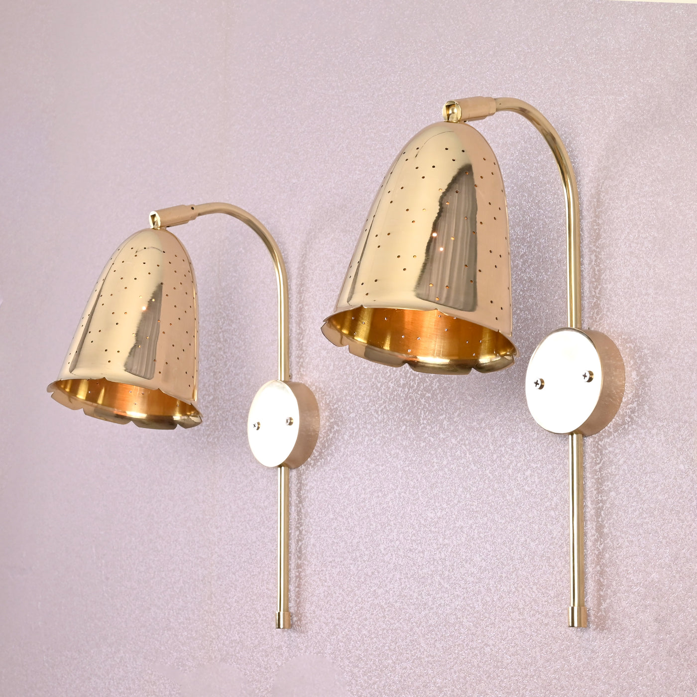 Pair of handcrafted brass bell-shaped wall sconces with perforated detailing mounted on light-colored wall