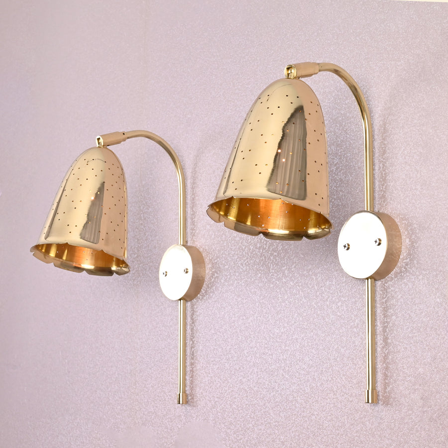 Pair of handcrafted brass bell-shaped wall sconces with perforated detailing mounted on light-colored wall