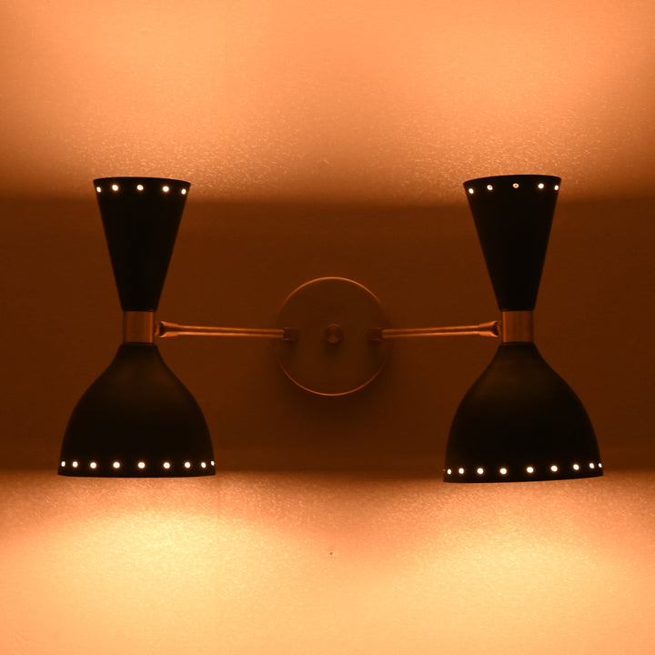 Double brass black wall sconce glowing with warm ambient light in dark setting