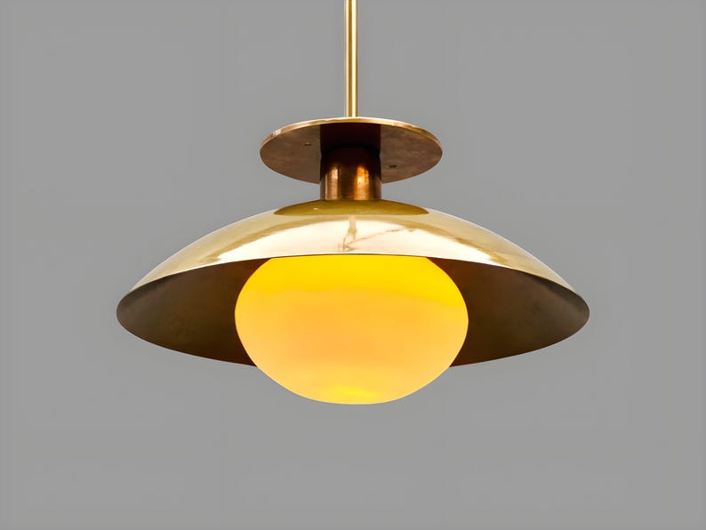 Handmade brushed brass bowl ceiling light glowing warmly with glass globe, modern minimalist brass lighting design