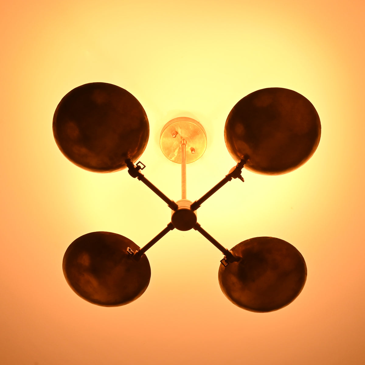Bottom-up glowing view of brass bowl chandelier, showing four darkened bowl interiors creating a warm halo lighting effect on the ceiling.