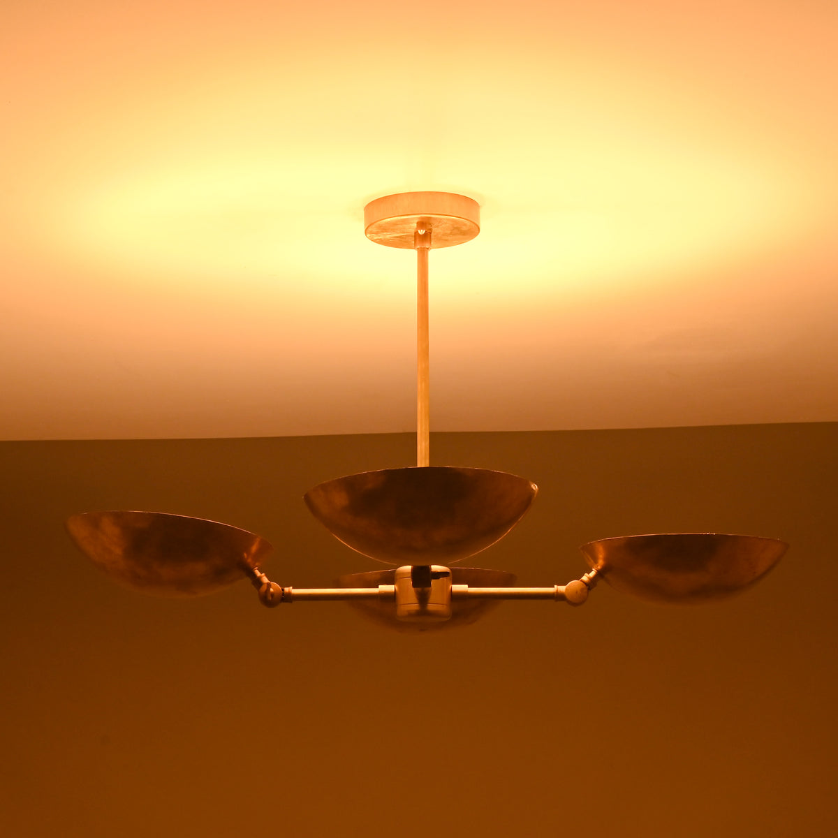 Brass bowl chandelier in warm ambient lighting, highlighting the golden hammered brass texture and soft upward illumination.