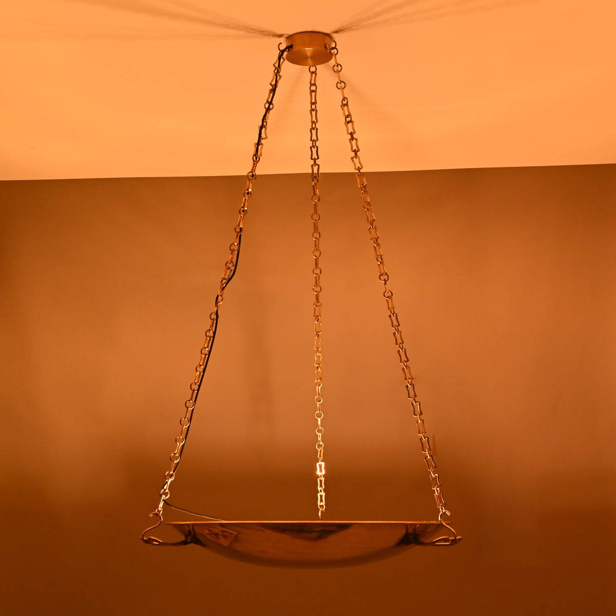 Chain-suspended brass bowl chandelier illuminated at night with warm ambient glow