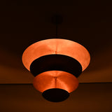 Night-shot of the brass bowl chandelier illuminated with warm indirect lighting across its stacked copper shades.