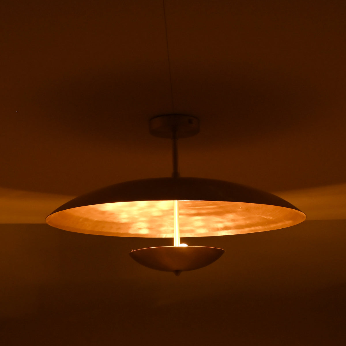 Warm brass ceiling light with bowl-shaped lower disc illuminated in a dark room